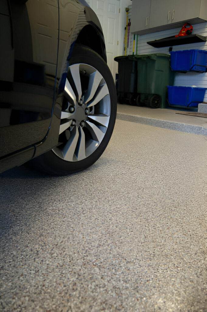 A car is parked in an Oregon garage featuring speckled concrete coating, surrounded by handy storage cabinets, recycling bins, and essential cleaning tools.