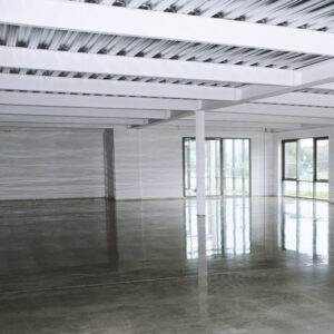 An empty industrial warehouse in Oregon features reflective concrete floors with a sleek coating and large windows, showcasing steel beams and a minimalist design.