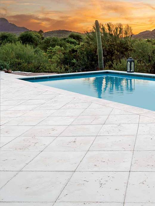 A pool with a white tiled deck, enhanced by sleek concrete coating, surrounded by desert greenery and a cactus, set against a stunning Oregon sunset sky.