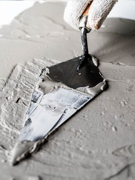 A gloved hand skillfully spreads gray mortar or cement, creating a flawless concrete coating with a trowel on a flat surface, reminiscent of the meticulous craftsmanship found in Oregon's construction sites.